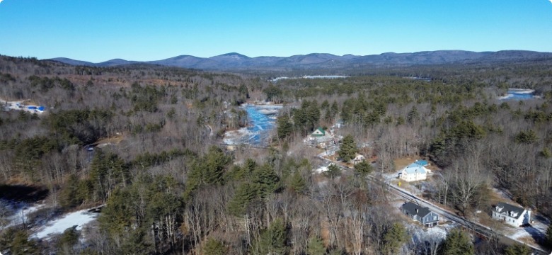 Aerial view of a river and homes along a road with hills beyond